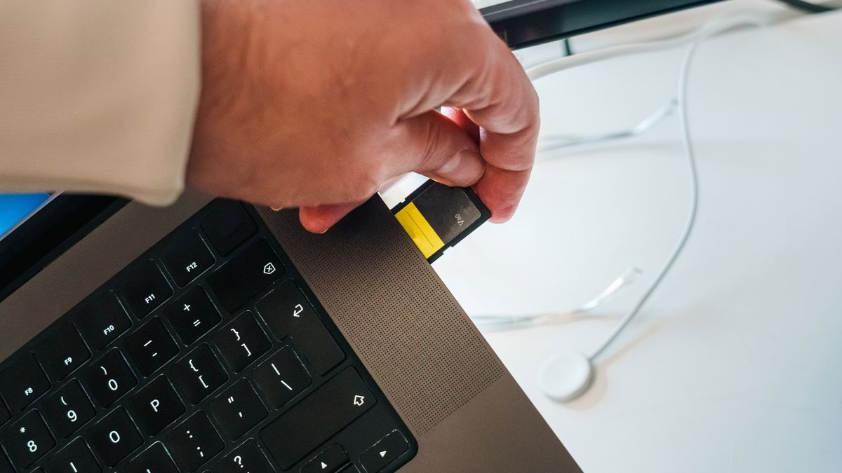 Tangan memasukkan kartu SD ke laptop untuk memindahkan file video